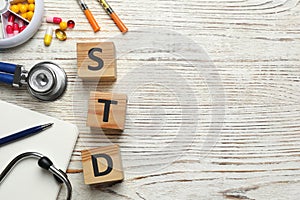 Flat lay composition with abbreviation STD and stethoscope on white wooden table. Space for text