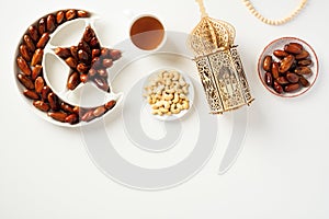 Flat lay composition with Arabic lantern, dried dates, nuts, cup of tea, rosary on white background. Ramadan Kareem concept