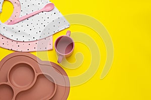 Flat lay composition with baby feeding accessories and bibs on yellow background, space for text