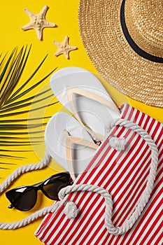 Flat lay composition with bag, palm leaf and other beach accessories on yellow background