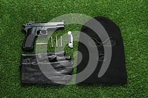 Flat lay composition with balaclava and weapons on green grass