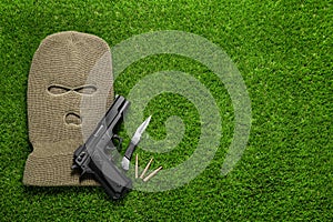 Flat lay composition with balaclava and weapons on grass. Space for text