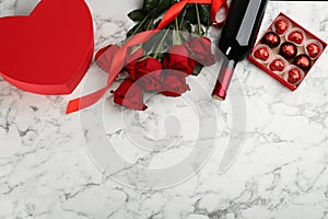 Flat lay composition with beautiful red roses and bottle of wine on white marble background, space for text. Valentine`s Day