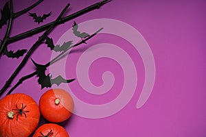 Flat lay composition with black branches, paper bats and pumpkins on purple background, space for text. Halloween celebration