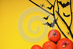 Flat lay composition with black branches, paper bats and pumpkins on yellow background, space for text. Halloween celebration
