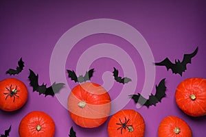 Flat lay composition with black paper bats and pumpkins on purple background, space for text. Halloween celebration