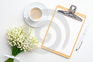 Flat lay composition with blank paper clipboard, coffee mug and bouquet of flowers lily of the valley, view from above. Wedding