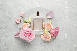 Flat lay composition with bottle of perfume and fresh flowers on light grey marble background