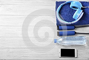 Flat lay composition with bottle of water, jumping rope, headphones and smartphone on wooden background. Gym workout