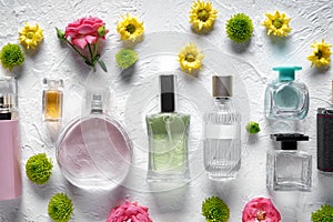 Flat lay composition with bottles of perfume and flowers on white textured background