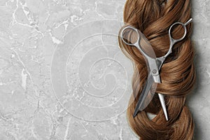 Flat lay composition with brown hair, scissors and space for text on grey background. Hairdresser