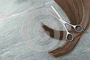 Flat lay composition with brown hair, thinning scissors and space for text on grey background.