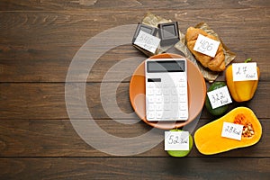 Flat lay composition of calculator and food products with calorific value tags on wooden table, space for text. Weight loss photo