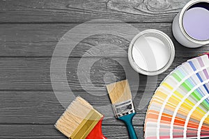 Flat lay composition with cans of paint, brushes and palette on grey wooden background