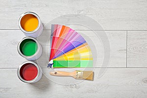 Flat lay composition with cans of paint, color palette samples and brush on wooden background.