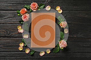 Flat lay composition with closed hardcover book and flowers on black table