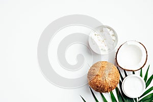 Flat lay composition with coconut body cream, coconut half, grated coconut in bowl and tropical palm leaf on white background. SPA