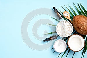 Flat lay composition with coconut oil cosmetics and tropical palm leaf on blue background. Top view coconut, green leaf, sliced