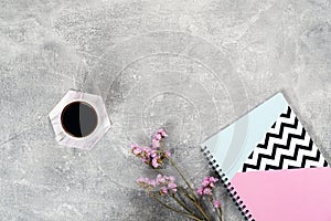 Flat lay composition with coffee cup, pink flowers, paper notebook on concrete surface. Top view female home office desk. Cozy