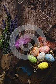 Flat lay composition of colourful painted easter eggs in a hay basket on wooden table. Happy Easter celebration