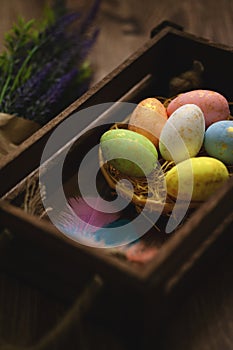 Flat lay composition of colourful painted easter eggs in a hay basket on wooden table. Happy Easter celebration