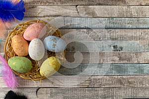 Flat lay composition of colourful painted easter eggs in a hay basket on wooden table. Happy Easter celebration