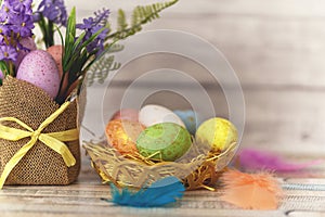 Flat lay composition of colourful painted easter eggs in a hay basket on wooden table. Happy Easter celebration