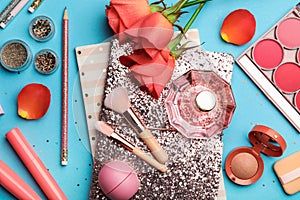 Flat lay composition with coral cosmetics and flowers on light blue