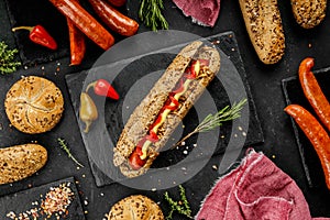 Flat lay composition of delicious hot dogs and sandwiches with different toppings on the dark background
