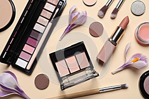 Flat lay composition with different makeup products and beautiful flowers on beige background