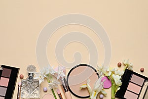 Flat lay composition with different makeup products and beautiful flowers on beige background, space for text