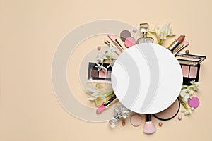 Flat lay composition with different makeup products, blank card and beautiful flowers on beige background, space for text