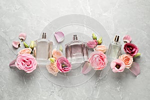 Flat lay composition of different perfume bottles and flowers on light grey marble background