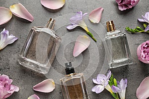 Flat lay composition of different perfume bottles, roses and freesia flowers on dark textured background