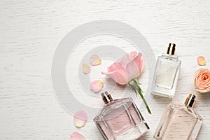 Flat lay composition with different perfume bottles and roses on white wooden background, space for text