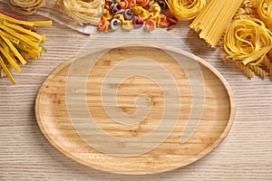 Flat lay composition with different types of pasta and plate on wooden background. Space for text