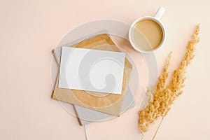 Flat lay composition with envelope, invitation card mockup, cup of coffee and dry flowers on beige background. Top view wedding