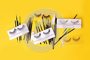 Flat lay composition with false eyelashes, cosmetic products and tools on trendy bright yellow background, concept of lashmakers
