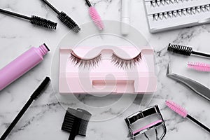 Flat lay composition with false eyelashes and tools on white marble table