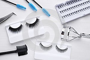 Flat lay composition with false eyelashes and tools on white wooden table