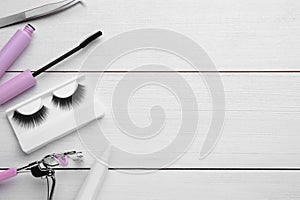 Flat lay composition with false eyelashes and tools on white wooden table. Space for text