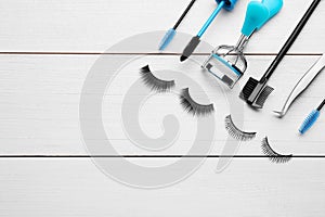 Flat lay composition with false eyelashes and tools on white wooden table. Space for text