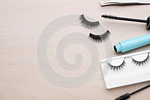 Flat lay composition with false eyelashes and tools on wooden table. Space for text