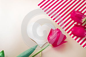 Flat lay composition with flowers and heart for mother's Day, greeting for women. Red tulips on pink background