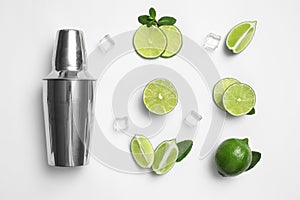 Flat lay composition with fresh juicy limes, ice cubes and cocktail shaker on background