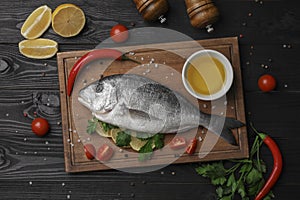 Flat lay composition with fresh raw dorado fish and spices on black wooden table