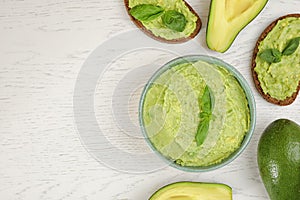 Flat lay composition with guacamole, sandwiches and avocados on wooden table. Space for text