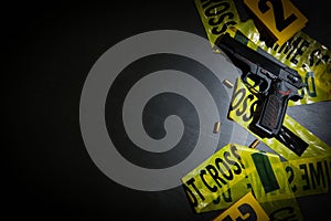 Flat lay composition with gun and crime scene tape on black slate background. Space for text