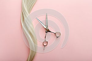 Flat lay composition with Hairdresser tools - scissors and strand of blonde hair on pink color background with copy space for text