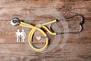 Flat lay composition with heart, stethoscope and paper silhouette of family on wooden background. Life insurance